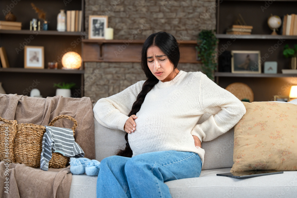 Pregnant woman experiencing contractions while sitting at home on the couch Pregnant woman experiencing contractions while sitting at home on the couch