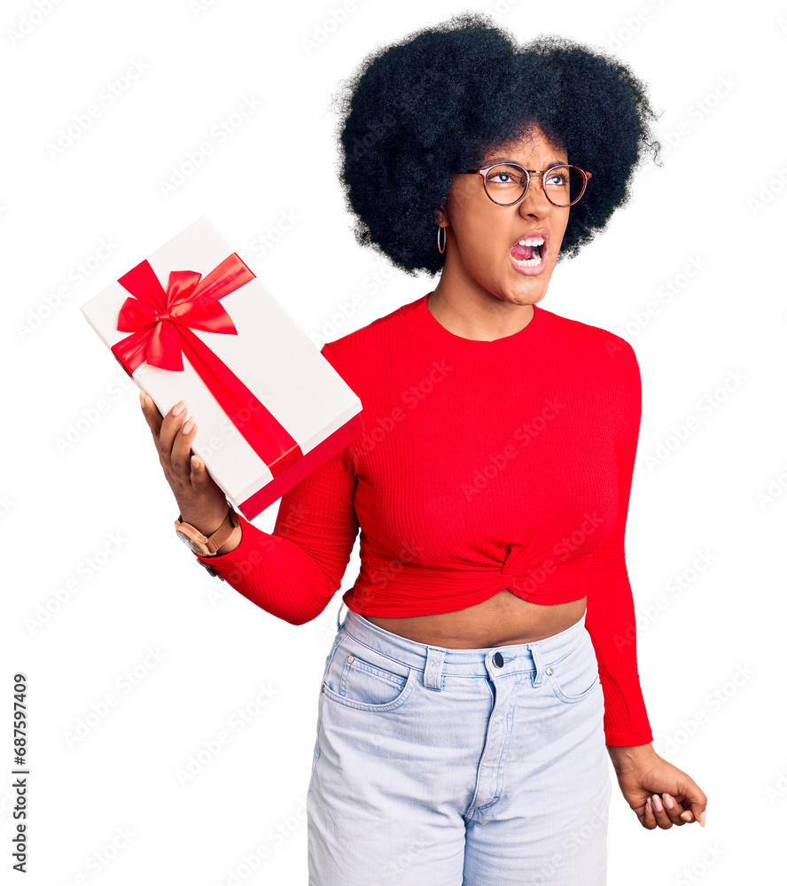 Young african american girl holding gift angry and mad screaming frustrated and furious, shouting with anger. rage and aggressive concept. Young african american girl holding gift angry and mad screaming frustrated and furious, shouting with anger. rage and aggressive concept.
