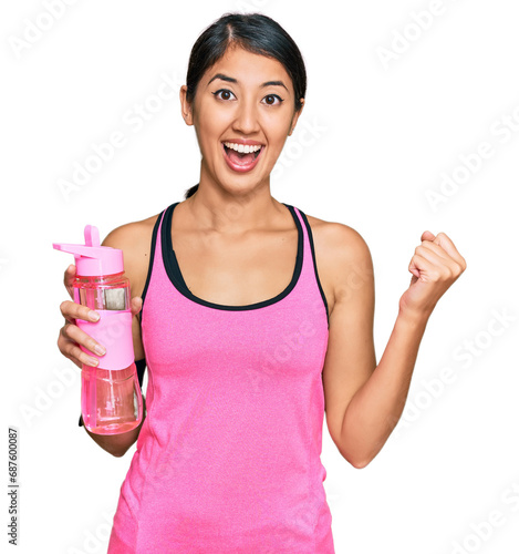 Beautiful asian young sport woman wearing sportswear drinking bottle of water screaming proud, celebrating victory and success very excited with raised arms