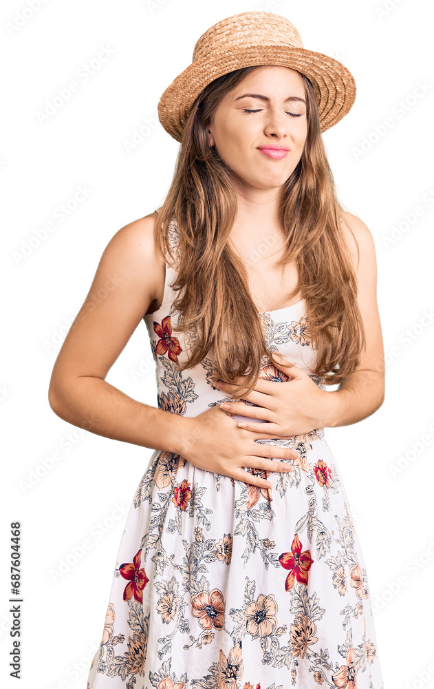 Beautiful caucasian young woman wearing summer hat with hand on stomach because indigestion, painful illness feeling unwell. ache concept.