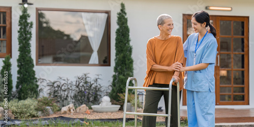 Nurse or caregiver help elderly walk by using walker in garden photo