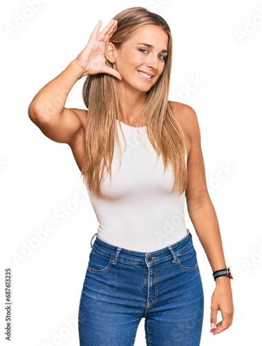 Young blonde woman wearing casual style with sleeveless shirt smiling with hand over ear listening an hearing to rumor or gossip. deafness concept.