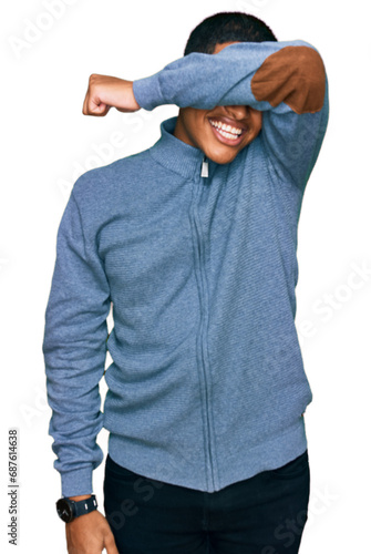 Young handsome hispanic man wearing casual sweatshirt covering eyes with arm smiling cheerful and funny. blind concept. © Krakenimages.com