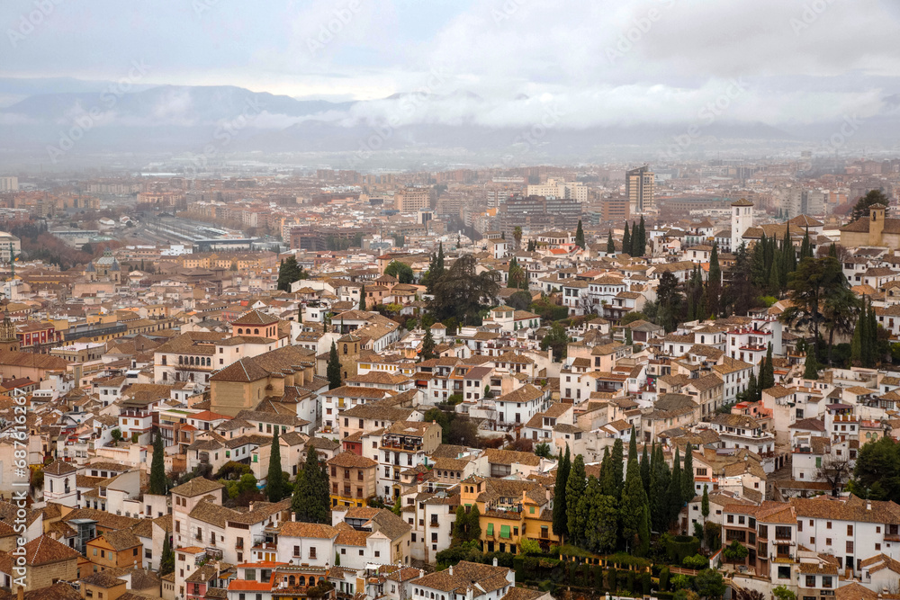 View of the city of Granada from the top of the hill where is the Alhambra Palace. City scenery against a cloud sky. Granada, Spain.