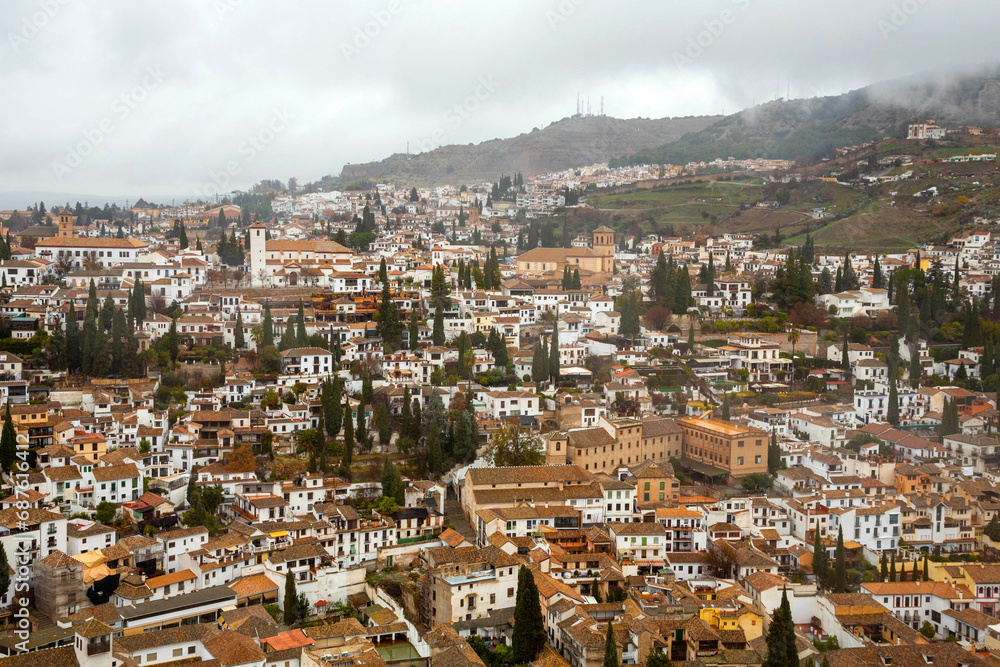 View of the city of Granada from the top of the hill where is the Alhambra Palace. The city landscape amidst mountains and cloudy skies. Granada, Spain.