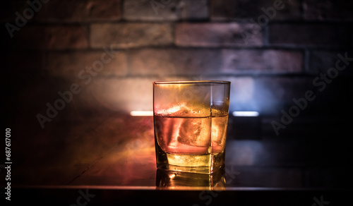 Whiskey in fire concept. Glass of whiskey and ice on wooden surface with color light and fog on background. Close up. Selective focus photo