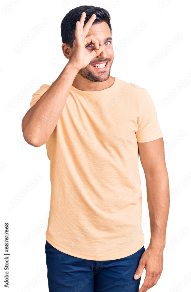 Young hispanic man wearing casual clothes doing ok gesture with hand smiling, eye looking through fingers with happy face. Young hispanic man wearing casual clothes doing ok gesture with hand smiling, eye looking through fingers with happy face.