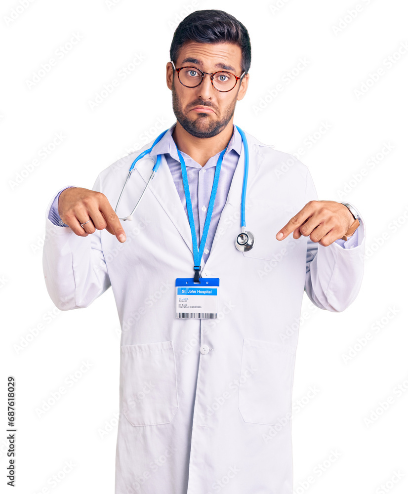 Young hispanic man wearing doctor uniform and stethoscope pointing down looking sad and upset, indicating direction with fingers, unhappy and depressed.