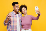 Young couple two friends family man woman of African American ethnicity wear purple casual clothes together do selfie shot on mobile cell phone show v-sign isolated on plain yellow orange background.