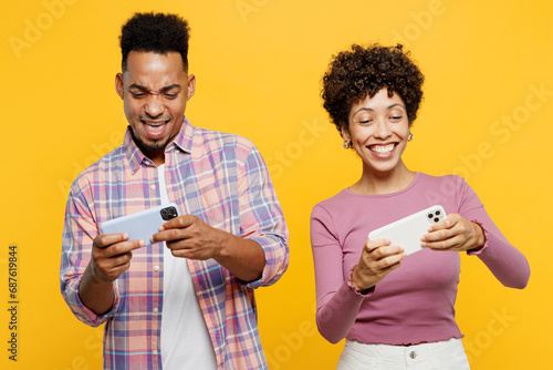 Young couple two friends family man woman wearing casual clothes together use play racing app on mobile cell phone hold gadget smartphone for pc video games isolated on plain yellow orange background.