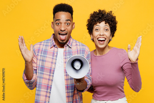 Young couple two friends family man woman of African American ethnicity wear casual clothes together hold megaphone scream announces discounts sale Hurry up isolated on plain yellow orange background.