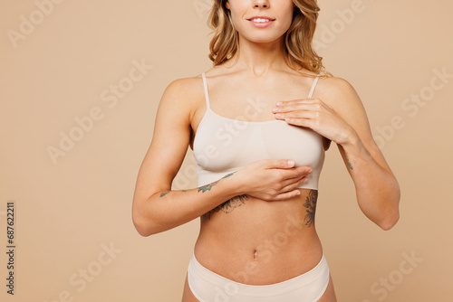 фотографія Close up cropped young nice lady woman with slim body perfect skin wearing nude top bra lingerie stand holding put hand on breast isolated on plain light beige background