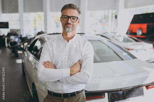 Adult happy man customer male buyer client wear shirt glasses hold hands crossed folded choose auto want to buy new automobile in car showroom vehicle salon dealership store motor show. Sales concept. © ViDi Studio