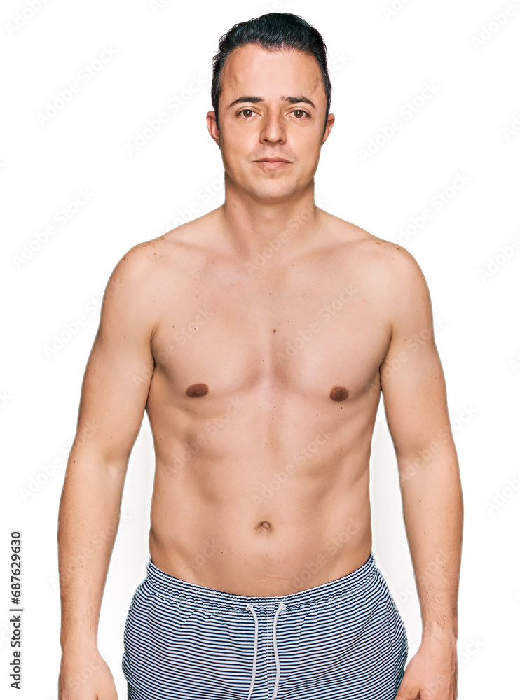 Handsome young man wearing swimwear shirtless relaxed with serious expression on face. simple and natural looking at the camera. Handsome young man wearing swimwear shirtless relaxed with serious expression on face. simple and natural looking at the camera.