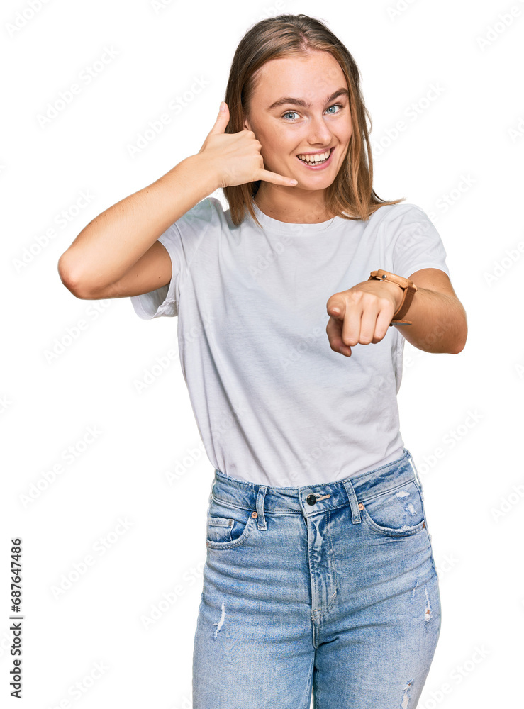 Beautiful young blonde woman wearing casual white t shirt smiling doing talking on the telephone gesture and pointing to you. call me. Beautiful young blonde woman wearing casual white t shirt smiling doing talking on the telephone gesture and pointing to you. call me.
