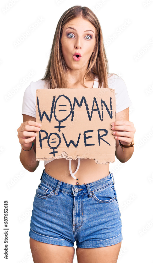 Young beautiful blonde woman holding woman power banner scared and amazed with open mouth for surprise, disbelief face Young beautiful blonde woman holding woman power banner scared and amazed with open mouth for surprise, disbelief face