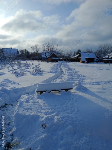 an old wooden bench covered with snow and a path cleared of snow
