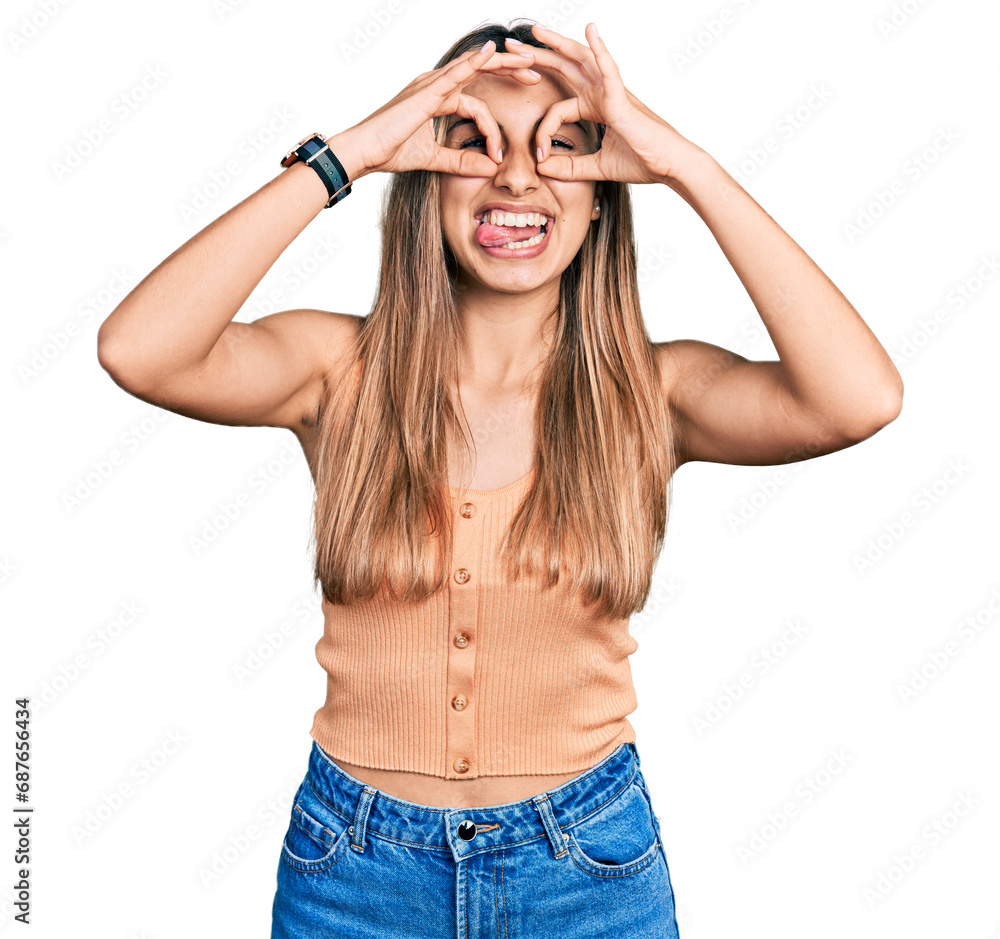Hispanic young woman wearing casual summer shirt doing ok gesture like binoculars sticking tongue out, eyes looking through fingers. crazy expression. Hispanic young woman wearing casual summer shirt doing ok gesture like binoculars sticking tongue out, eyes looking through fingers. crazy expression.