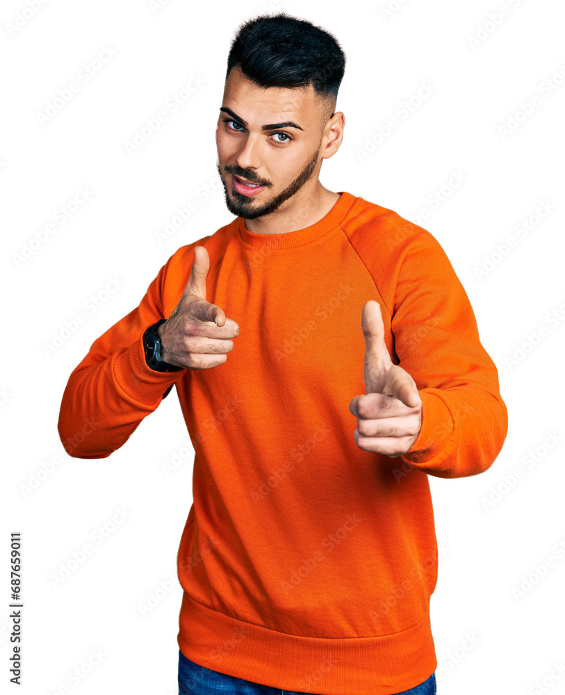 Young hispanic man with beard wearing casual orange sweater pointing fingers to camera with happy and funny face. good energy and vibes. Young hispanic man with beard wearing casual orange sweater pointing fingers to camera with happy and funny face. good energy and vibes.