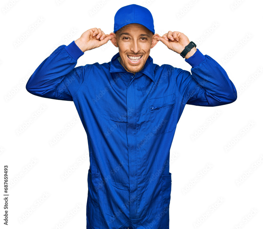 Bald man with beard wearing builder jumpsuit uniform smiling pulling ears with fingers, funny gesture. audition problem Bald man with beard wearing builder jumpsuit uniform smiling pulling ears with fingers, funny gesture. audition problem