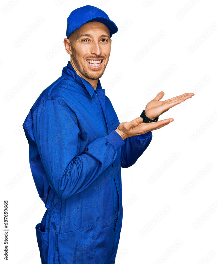 Bald man with beard wearing builder jumpsuit uniform pointing aside with hands open palms showing copy space, presenting advertisement smiling excited happy