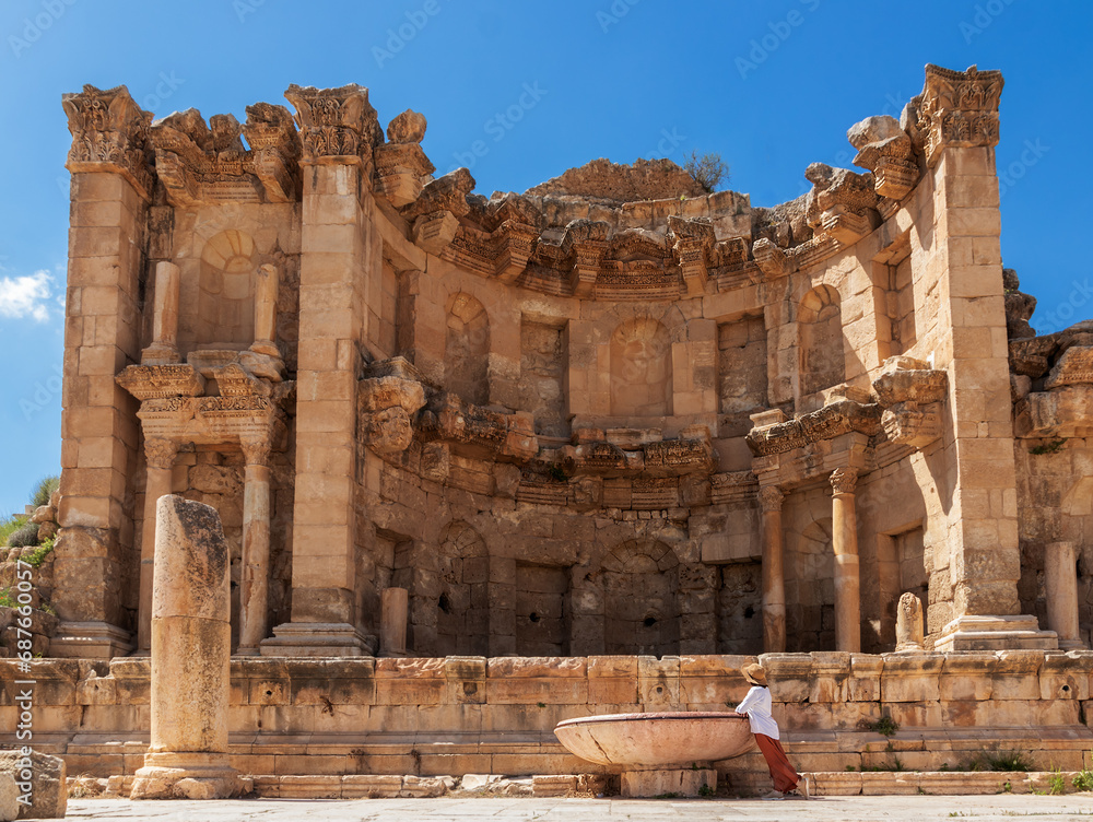 Woman tourist leaning on the Nymphaeum fountain on a sunny day during her sightseeing trip in Jerash