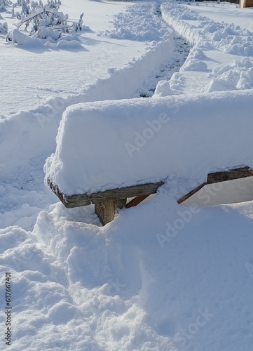 an old wooden bench covered with snow and a path cleared of snow

