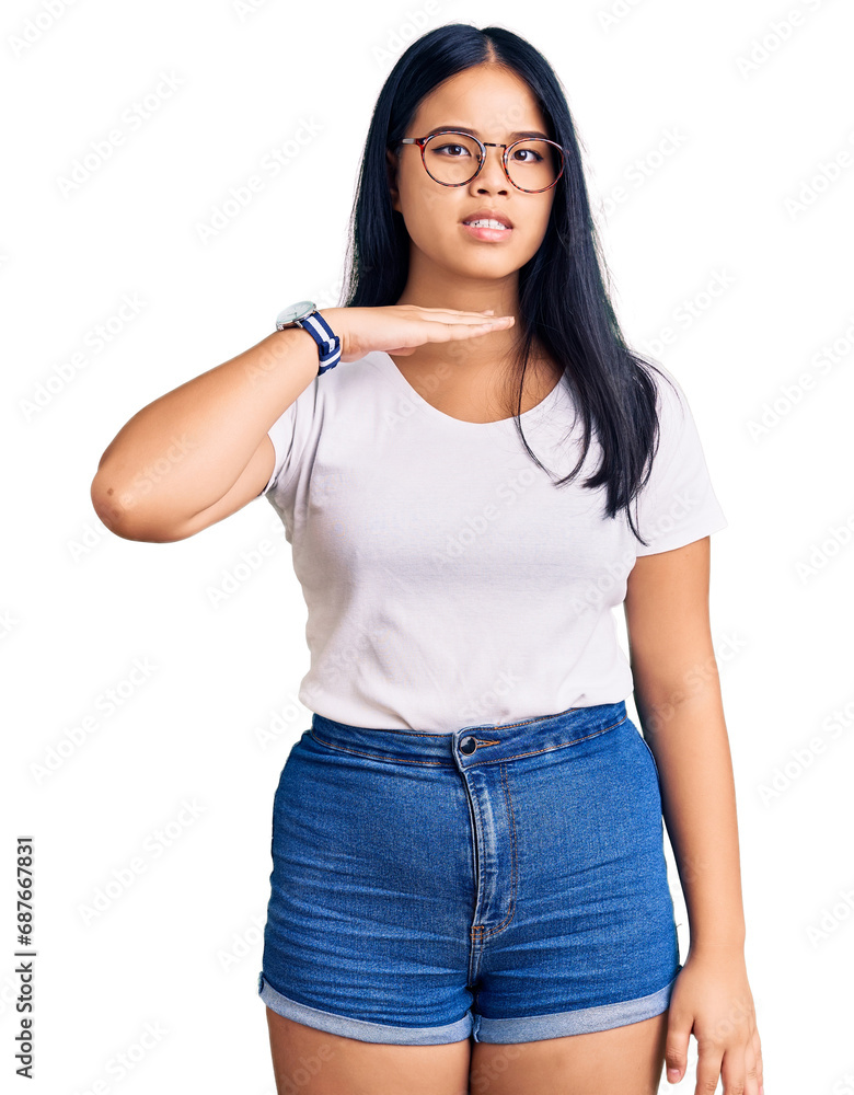 Young beautiful asian girl wearing casual clothes and glasses cutting throat with hand as knife, threaten aggression with furious violence Young beautiful asian girl wearing casual clothes and glasses cutting throat with hand as knife, threaten aggression with furious violence
