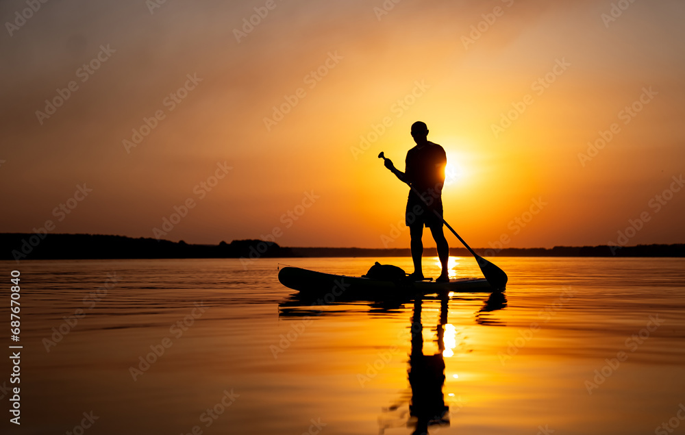 A Serene Moment: Man Standing on Paddle Board in the Glistening Water. A man standing on a paddle board in the water
