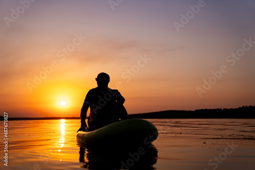 A Serene Moment: A Man Contemplating Life on a Raft as the Sun Sets. A man sitting on a raft in the water at sunset