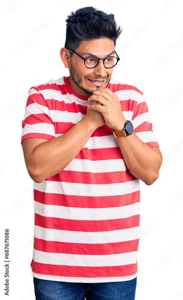 Handsome latin american young man wearing casual clothes and glasses laughing nervous and excited with hands on chin looking to the side Handsome latin american young man wearing casual clothes and glasses laughing nervous and excited with hands on chin looking to the side