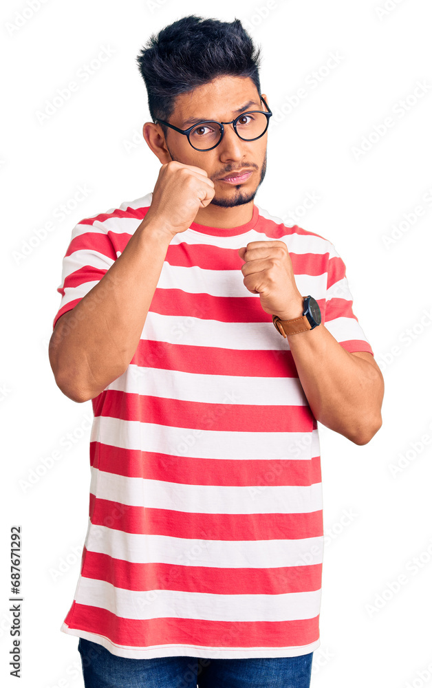 Handsome latin american young man wearing casual clothes and glasses ready to fight with fist defense gesture, angry and upset face, afraid of problem Handsome latin american young man wearing casual clothes and glasses ready to fight with fist defense gesture, angry and upset face, afraid of problem