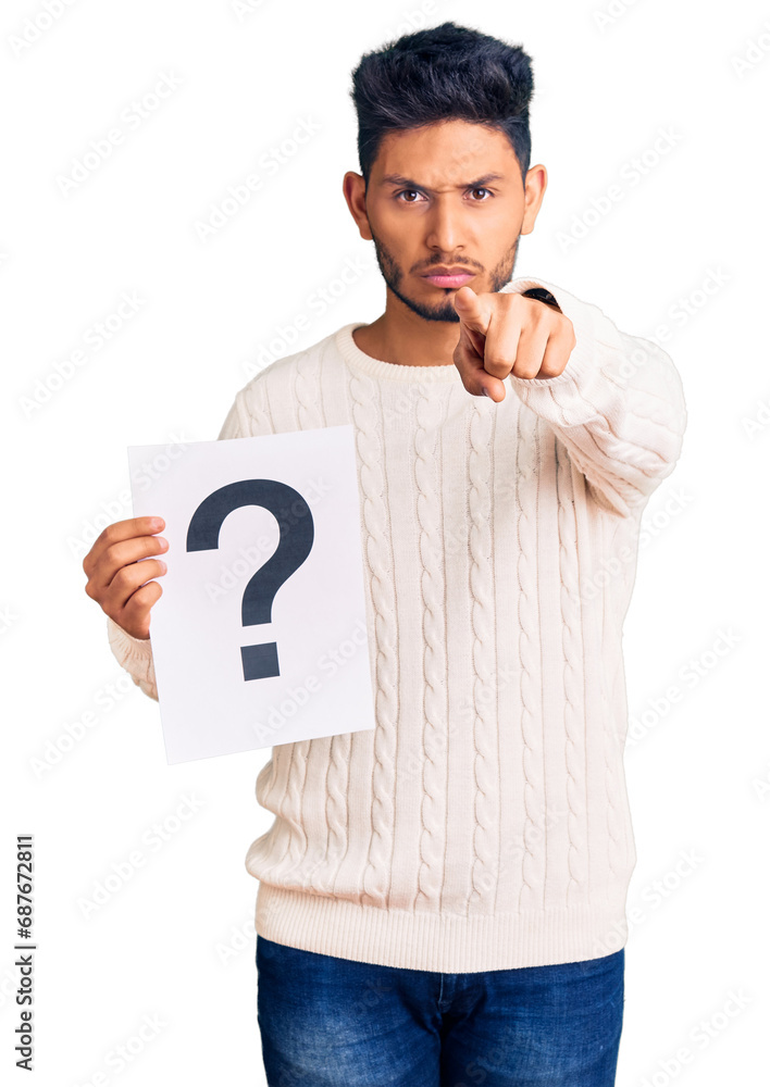Handsome latin american young man holding question mark pointing with finger to the camera and to you, confident gesture looking serious Handsome latin american young man holding question mark pointing with finger to the camera and to you, confident gesture looking serious