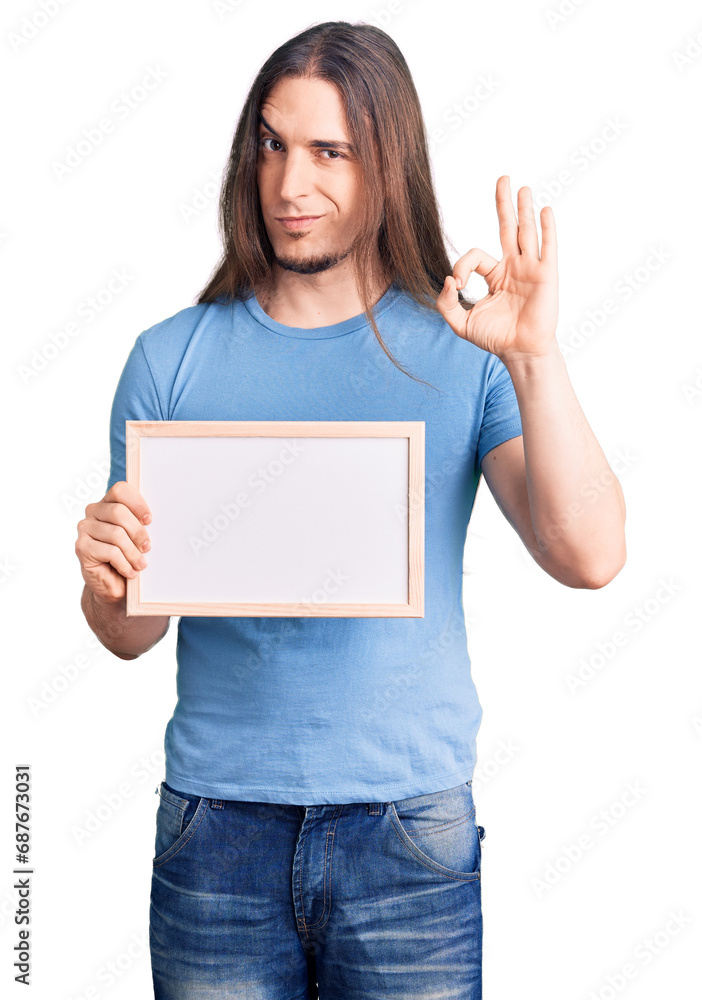 Young adult man with long hair holding empty white chalkboard doing ok sign with fingers, smiling friendly gesturing excellent symbol Young adult man with long hair holding empty white chalkboard doing ok sign with fingers, smiling friendly gesturing excellent symbol