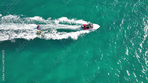 Aerial drone video of extreme inflatable towable tube cruising in high speed attached on powerboat with children riding, watersport photo