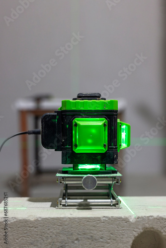 Glowing green laser spirit level built on a brick at a construction site with green lines. Accurate measurement of construction in the house