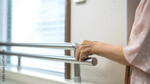 Gros plan sur une main d'une personne âgée s'appuyant sur une barre d'appui en métal près d'une fenêtre dans une maison de retraite.