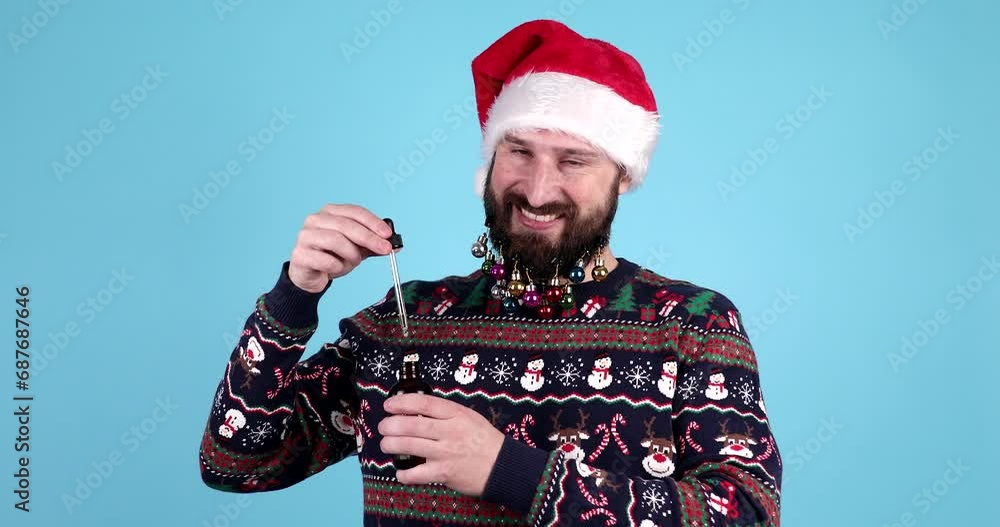 Bearded man in christmas sweater and santa hat holding pipette with beard oil. Bearded man in christmas sweater and santa hat holding pipette with beard oil.