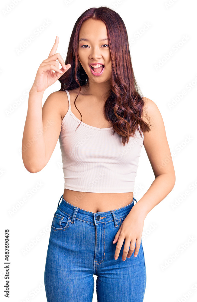 Young beautiful chinese girl wearing casual clothes pointing finger up with successful idea. exited and happy. number one. Young beautiful chinese girl wearing casual clothes pointing finger up with successful idea. exited and happy. number one.