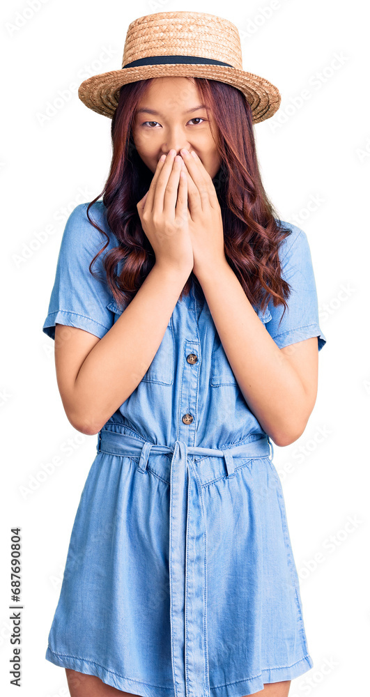 Young beautiful chinese girl wearing summer hat laughing and embarrassed giggle covering mouth with hands, gossip and scandal concept Young beautiful chinese girl wearing summer hat laughing and embarrassed giggle covering mouth with hands, gossip and scandal concept