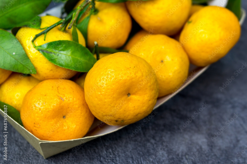 orange tangerines with green leaves in a cardboard tray on a table orange tangerines with green leaves in a cardboard tray on a table
