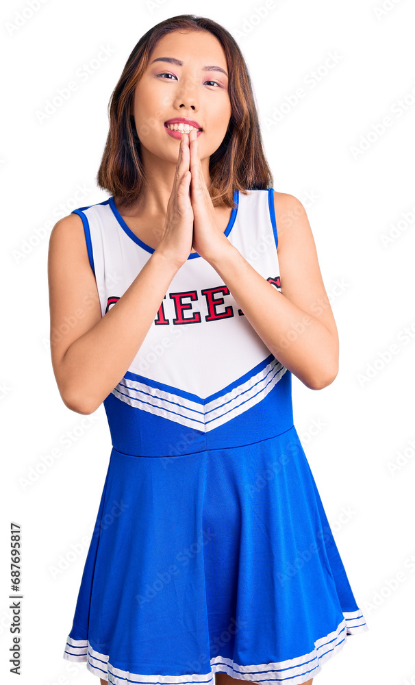 Young beautiful chinese girl wearing cheerleader uniform praying with hands together asking for forgiveness smiling confident. Young beautiful chinese girl wearing cheerleader uniform praying with hands together asking for forgiveness smiling confident.