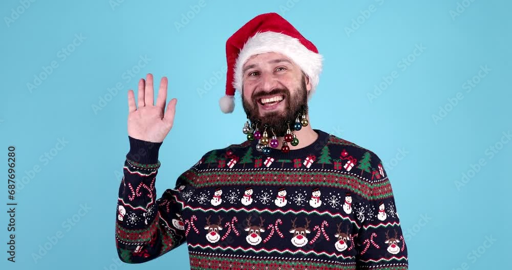 Hello! Portrait of positive handsome bearded man in santa hat and sweater waving raised hand and saying hi to camera, christmas time. Hello! Portrait of positive handsome bearded man in santa hat and sweater waving raised hand and saying hi to camera, christmas time.