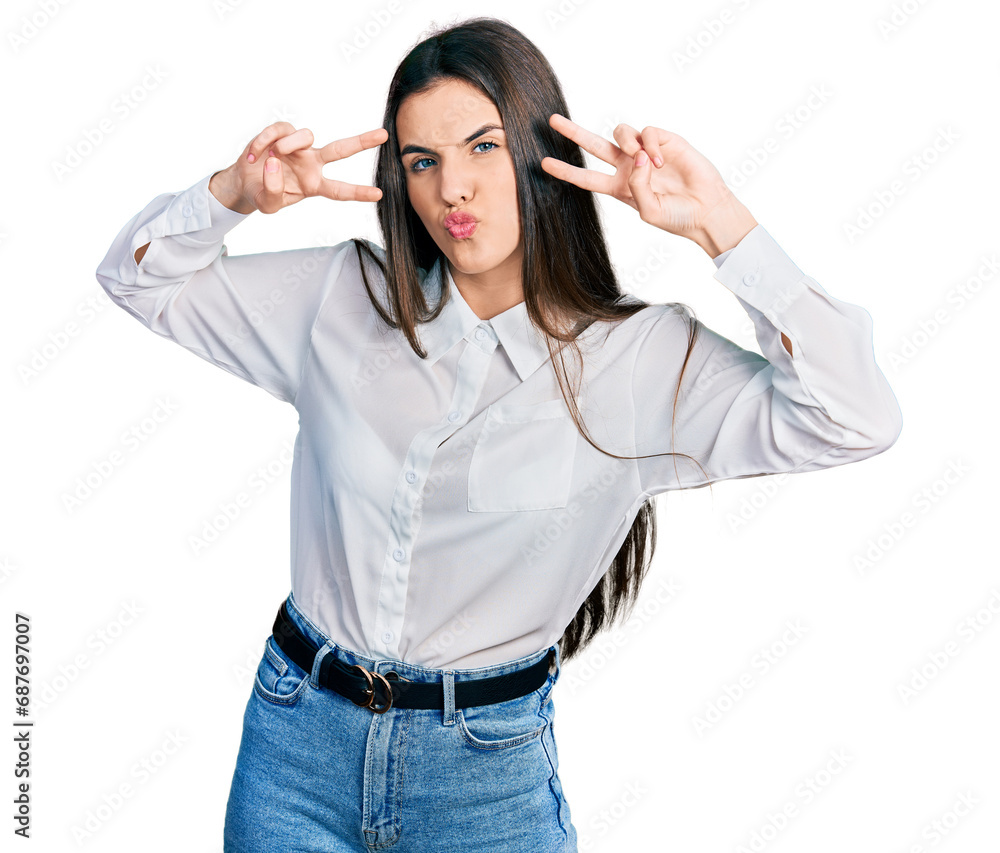 Young brunette teenager doing peace gesture close to eyes looking at the camera blowing a kiss being lovely and sexy. love expression. Young brunette teenager doing peace gesture close to eyes looking at the camera blowing a kiss being lovely and sexy. love expression.