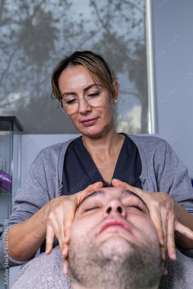 Obraz premium Vertical photo of a woman giving a facial massage to a client in a beauty salon.
