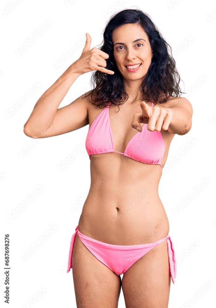 Fototapeta premium Young beautiful hispanic woman wearing bikini smiling doing talking on the telephone gesture and pointing to you. call me.