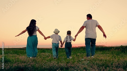 Parents and kids have fun in nature enjoying fresh air. Big family. Father and mother run with children through grassy meadow in summertime. Family play with son, daughter spending weekends together.