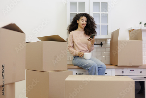 moving to new apartment relocation. happy young woman, packing boxes with personal belongings, African American lady calls transportation service and drinks tea, moving service © MyJuly