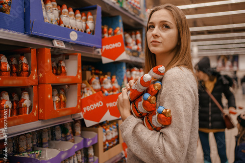 Stack of Chocolate Santa Clauses. Christmas time. A young woman chooses a gift set for Christmas to a child on a supermarket shelf.