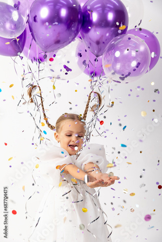 little girl blonde in a white dress catches confeti smiling happy on white background, holiday concept. A child is celebrating a birthday on a white background